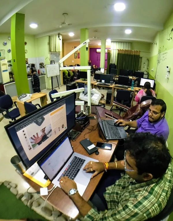 People working at laptops and monitors in an office with green walls.