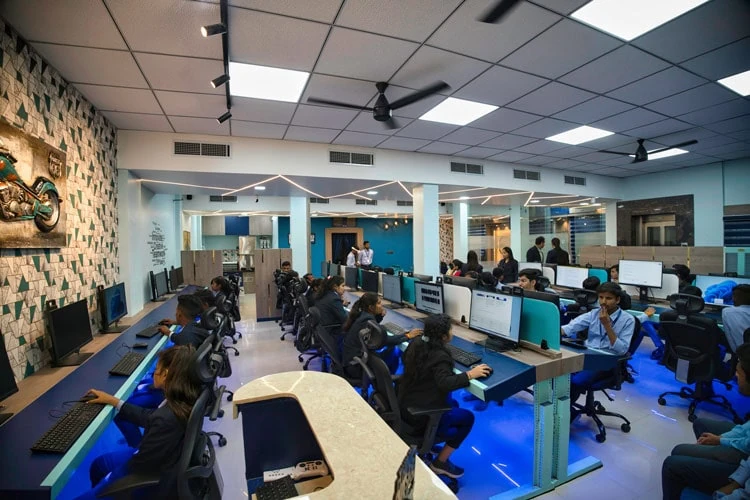 People at desktop workstations in an open office with glass partitions.